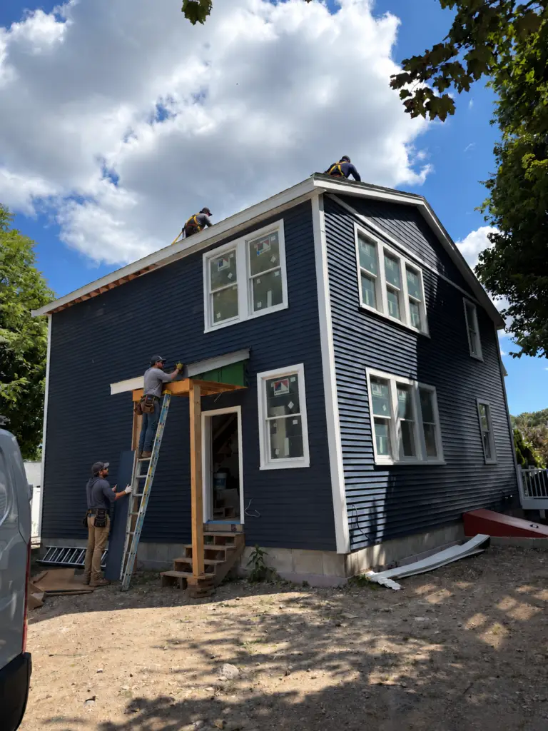 Roofers and siding installers completing the exterior building envelope of a blue residential addition