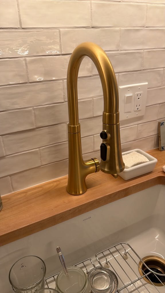 Brass colored kitchen faucet against a light tile backsplash
